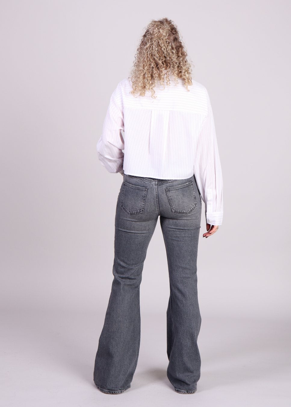 Achterkant grijze flared homage jeans op model met witte blouse